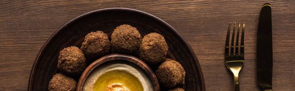 top view of falafel balls with hummus on plate near cutlery on wooden table, panoramic shot - Фото, изображение