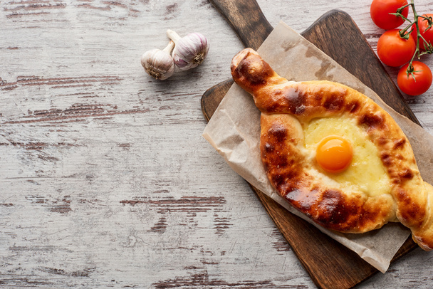 Top view of adjarian khachapuri with tomatoes and garlic on table - Foto, afbeelding