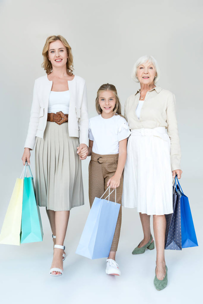 Lächelnde Enkelin, Großmutter und Mutter mit Einkaufstüten auf grauem Hintergrund  - Foto, Bild