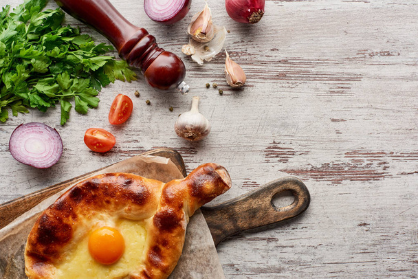Top view of pepper mill with adjarian khachapuri and vegetables on wooden table - Photo, image
