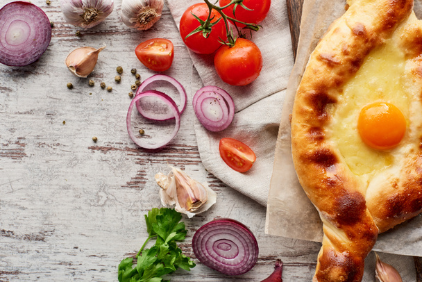 Top view of adjarian khachapuri with vegetables and greens on wooden table - Photo, image