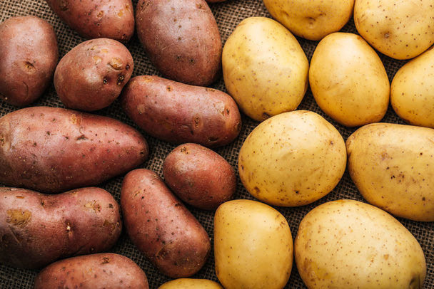 bovenaanzicht van biologische rauwe aardappelen op bruin rustieke zak - Foto, afbeelding
