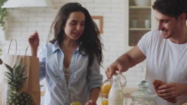Happy couple cooking breakfast at home. Young married couple eating croissant. - Filmagem, Vídeo