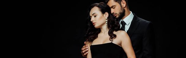 panoramic shot of handsome man with closed eyes standing with attractive girlfriend isolated on black  - Photo, Image