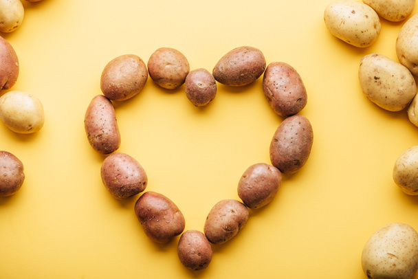 top view of raw whole fresh potatoes arranged in heart on yellow background - 写真・画像