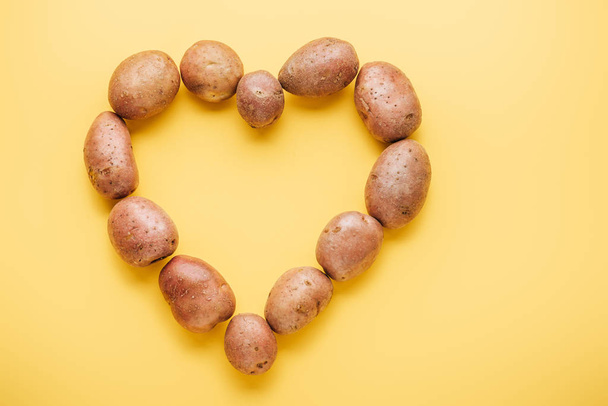 top view of raw whole fresh potatoes arranged in heart on yellow background - 写真・画像