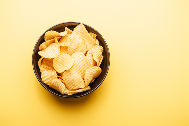 top view of delicious crispy potato chips in bowl on yellow background - Foto, Bild