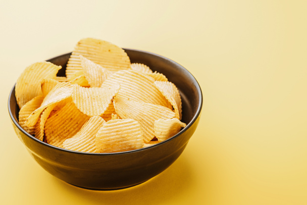 delicious crispy potato chips in bowl on yellow background - Photo, Image