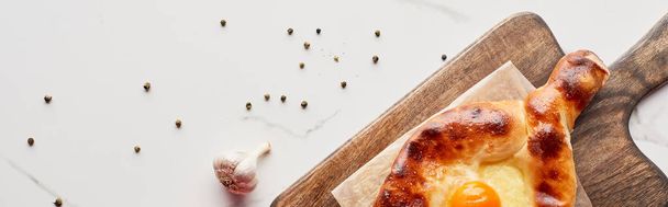 Adjarian khachapuri on cutting board with garlic and pepper on marble texture, panoramic shot - Foto, imagen