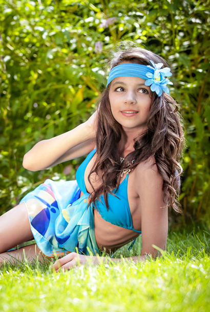 Portrait of beautiful cute brunette teenager model with makeup, poreo, in summer colorful swimsuit posing on the sea coast. young young girl in a bathing suit lying on the grass. Selective focus - Foto, Imagem