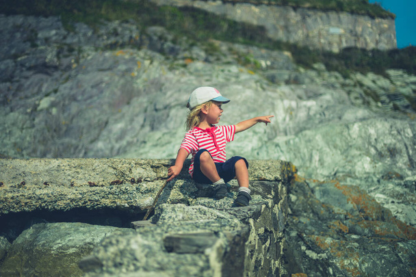 A little toddler is sitting on a rock by the sea - Foto, afbeelding