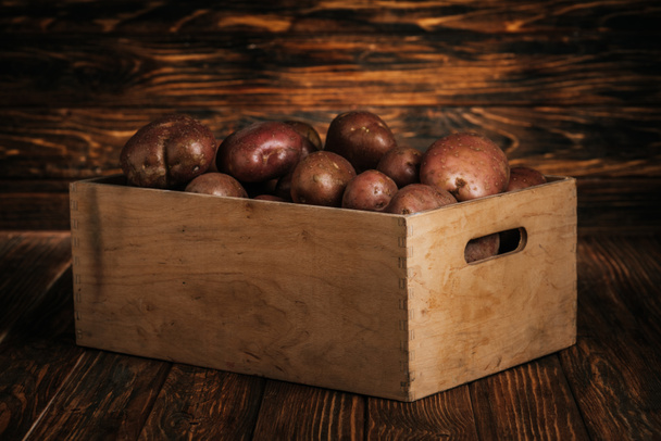 fresh ripe potatoes in box on wooden background - Фото, изображение