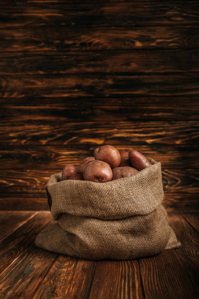 ripe potatoes in rustic sack on wooden background - Fotó, kép