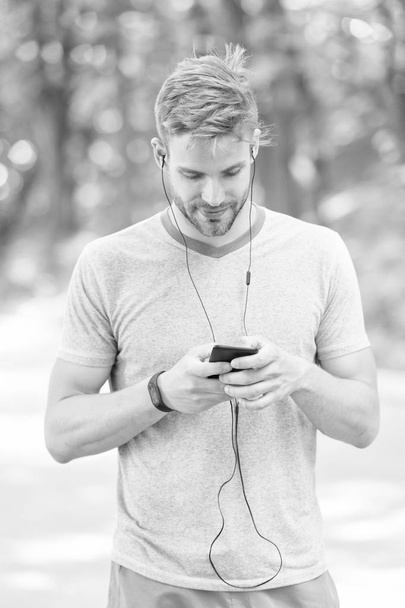 Pairing his fitness watch with his smartphone. Sportsman using fitness tracker for training outdoor. Fit man tracking his fitness activity with sports watch. Monitoring his health with fitness device - Foto, Imagem