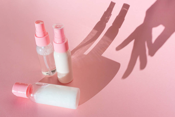 Frascos cosméticos transparentes sobre fondo rosa con sombras espectaculares. También la sombra de una mano femenina. El concepto de cosmetología, la elección de los cosméticos, la cara y el cuidado de la piel del cuerpo. Minimalismo
. - Foto, Imagen