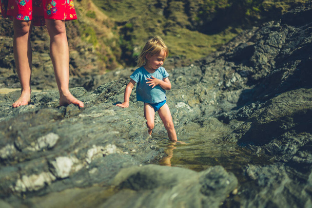 A little toddler is playing in rockpools on the beach with his mother - Fotoğraf, Görsel