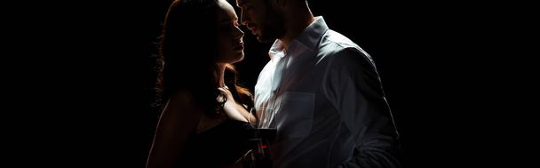 panoramic shot of bearded man standing with woman holding glass of red wine isolated on black  - Photo, Image