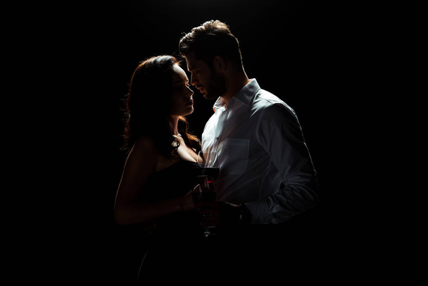 hombre guapo de pie con la mujer sosteniendo vaso de vino tinto aislado en negro
  - Foto, Imagen