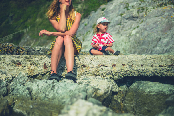Een jonge moeder en haar peuter ontspannen zich in de zomer op rotsen aan zee. - Foto, afbeelding