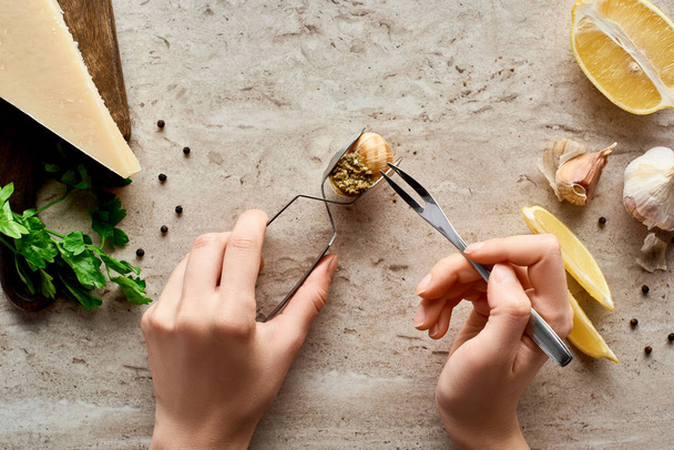 partial view of woman eating delicious cooked escargots with tweezers on stone background near ingredients - Photo, Image