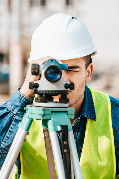 Surveyor en hardhat y chaqueta de alta visibilidad buscando a lo largo del nivel digital
  - Foto, Imagen