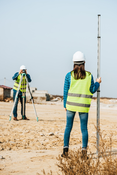 Selective focus of surveyors with survey ruler and digital level on construction site - Photo, Image