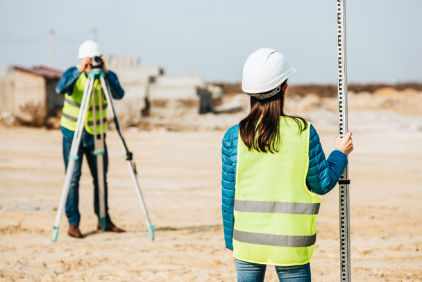 Selective focus of surveyor holding ruler and colleague with digital level on background - Photo, Image