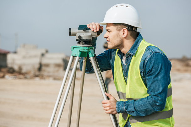 Side view of surveyor in hardhat looking throughout digital level on construction site - Foto, Imagem