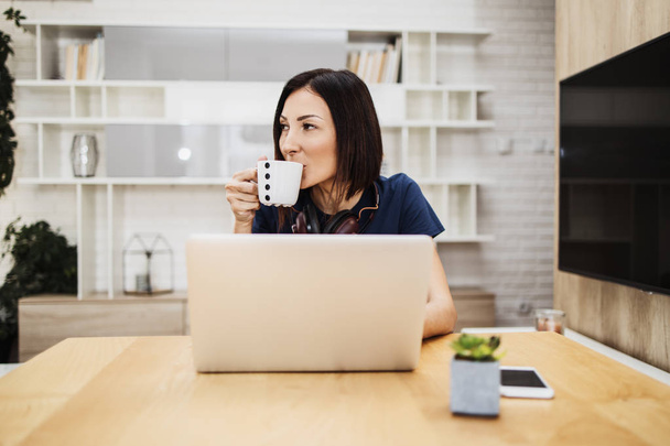 Attractive and happy middle age female freelancer is working and smiling at her home. Modern living room in background. Freelancing job concept. - Φωτογραφία, εικόνα
