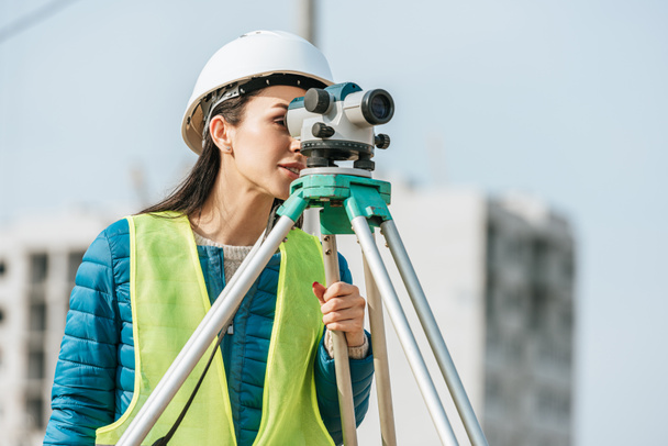 Surveyor in hardhat and high visibility jacket looking in digital level - Fotó, kép