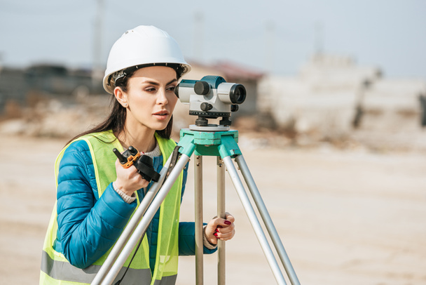 Female surveyor with radio set looking through digital level  - Photo, Image