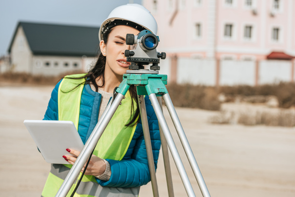 Жіночий геодезист з цифровим планшетом, який дивиться через рівень вимірювання
 - Фото, зображення