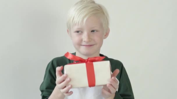 ξανθό αγόρι κρατά ένα όμορφα τυλιγμένο δώρο στην κάμερα - Πλάνα, βίντεο