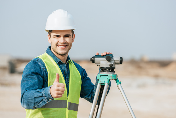 Smiling surveyor with digital level showing thumb up gesture - Photo, Image