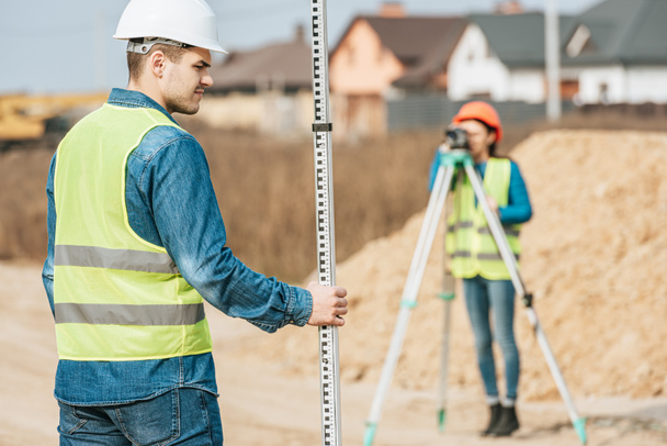 Selective focus of surveyor with ruler and colleague with digital level on background - Photo, Image