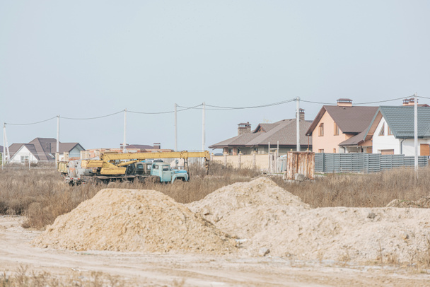 Moldes de arena en camino de tierra con grúa de construcción y casas en el fondo
 - Foto, Imagen