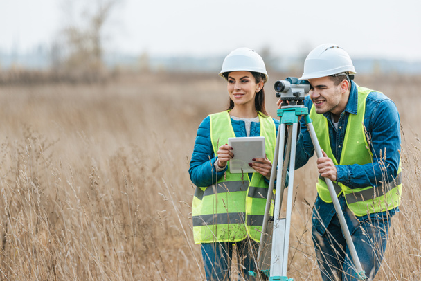 Smiling surveyors with digital level and tablet in field - Photo, Image