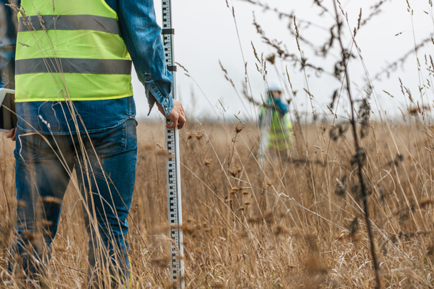 Selective focus of surveyor with ruler and colleague with digital level in field - Photo, Image