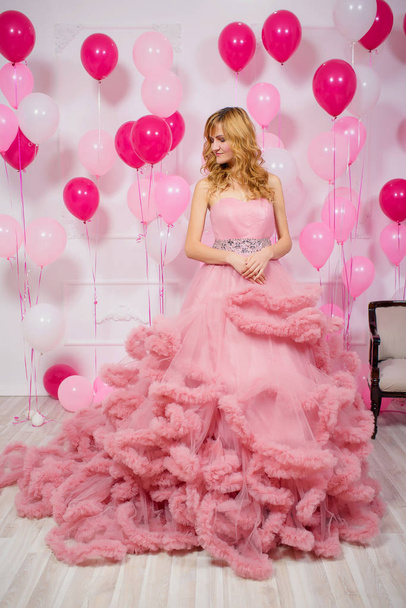 A young woman in a pink ball gown on a background of balloons. Beautiful girl in evening puffy Cloud dress with pink and white balloons. Air lush ball gown on the girl - Фото, зображення