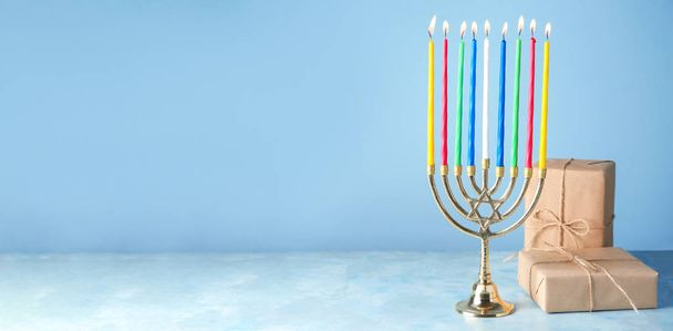 Menorah and gifts for Hanukkah on table against color background with space for text - Photo, Image