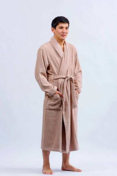 Asian male in a beige Bathrobe on a white background. Men's Bathrobe large. Bathrobe beige color on the man - Photo, Image