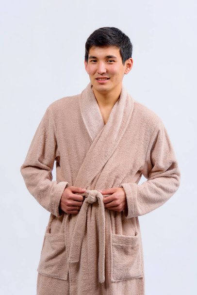 Азиатский самец в бежевом халате на белом фоне. Мужской халат большой. Халат бежевого цвета на человеке
 - Фото, изображение