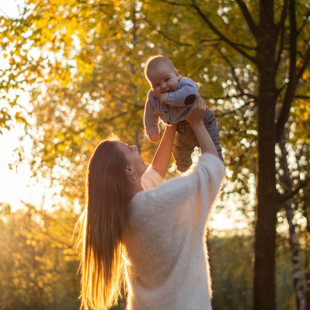 Gelukkige familie op herfstwandeling. Moeder houdt zoontje in haar armen en geniet van de prachtige herfstnatuur in een park.  - Foto, afbeelding