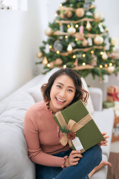 Beautiful asian woman in casual sweater holding gift near decora - Zdjęcie, obraz
