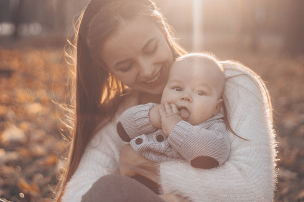 Счастливая семья на осенней прогулке. Мать держит маленького сына на руках и наслаждается красивой осенней природой в парке
.  - Фото, изображение