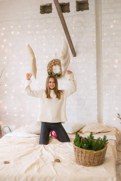 Cute teenage girl has fun at home in a light loft on the bed, decorated for Christmas with garlands and needles. Christmas mood - Photo, image