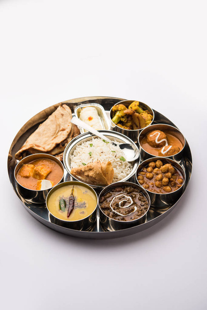 Indian vegetarian Food Thali or platter includes paneer butter masala, dal makhani / tarka, chole papad, kofta curry, gulab jamun, aloo-gobi sabji, chapati and rice with Bengali sweet served - Photo, Image