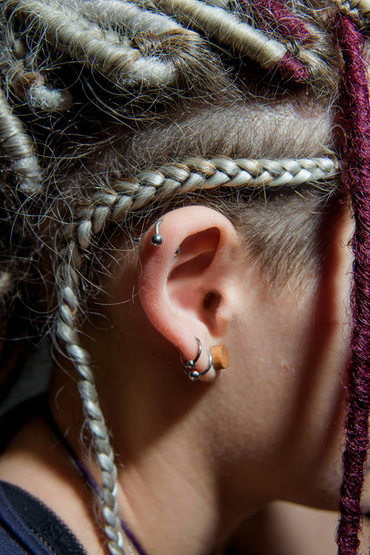 Piercing op het oor van een meisje met dreadlocks. Vrouwelijk oor met de oorbellen van dichtbij. Details van het beeld van het meisje van de informele cultuur - Foto, afbeelding