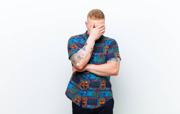 young blonde man wearing a cool shirt looking puzzled and confused, insecure and pointing in opposite directions with doubts against white background - Fotó, kép