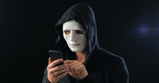 フードの匿名のマスク詐欺師は、スマートフォンを使用して恐喝の身代金を要求します。マスク犯罪者は、携帯電話を使用してSmsを介して脅威の助けを借りて被害者を脅迫します. - 映像、動画